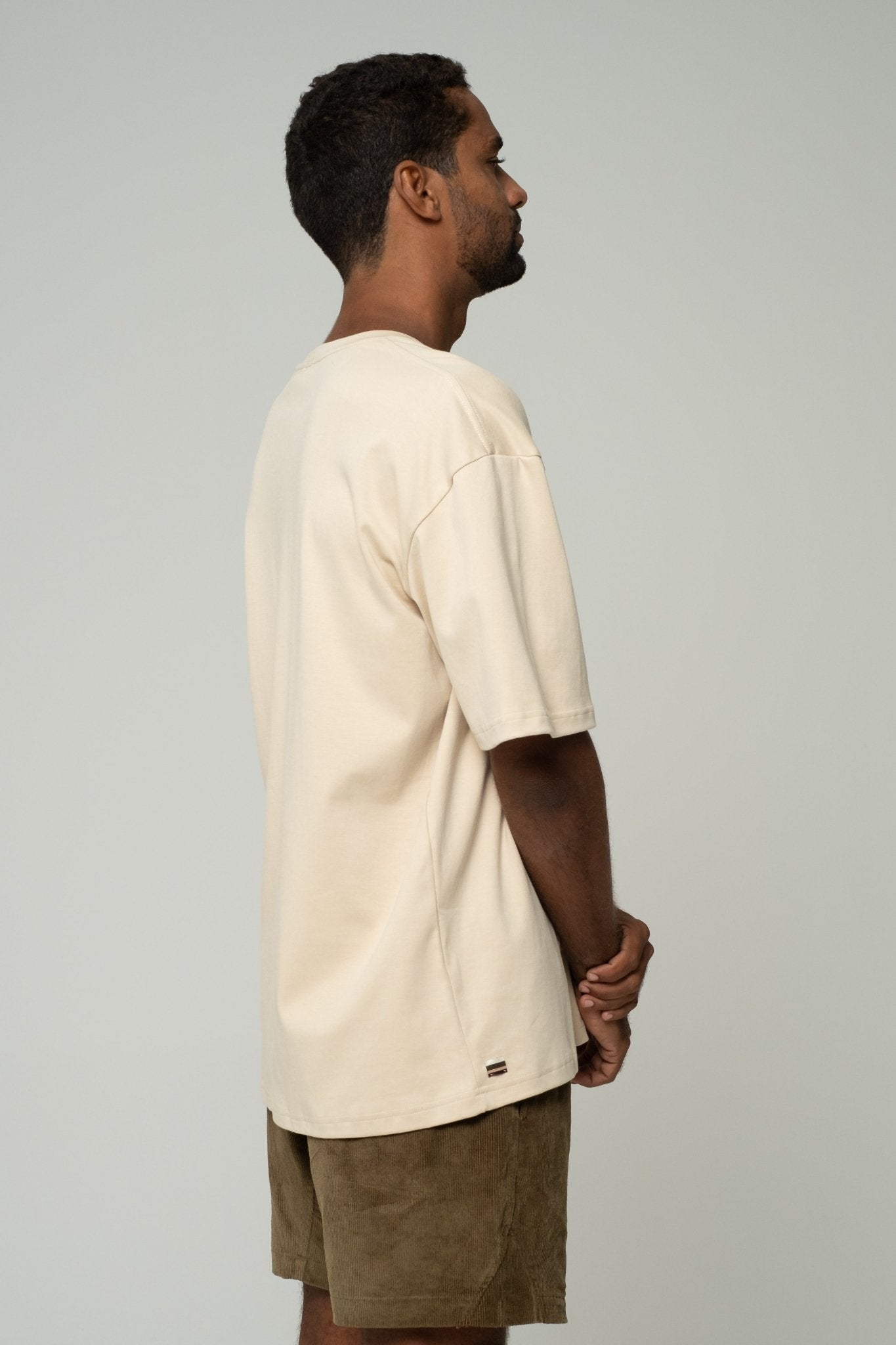 alt="Side profile of Kavash off‑white oversized t‑shirt showing dropped shoulder and relaxed drape."