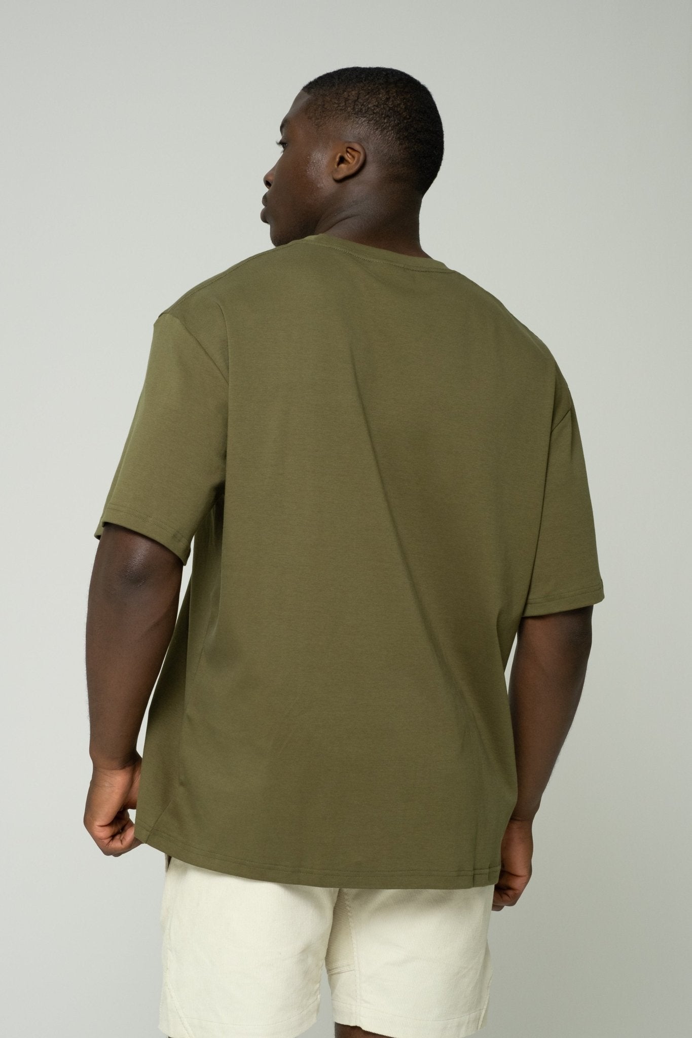 alt="Side profile of Kavash dark green Vos oversized t‑shirt showing dropped shoulder and relaxed drape."