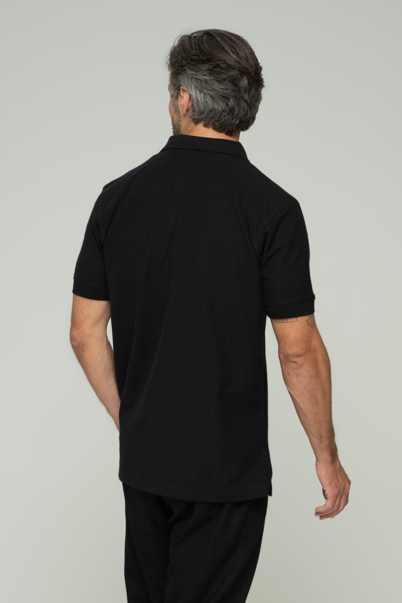 alt="Detail of ASASI black polo shirt sleeve and stitching, soft cotton pique fabric."